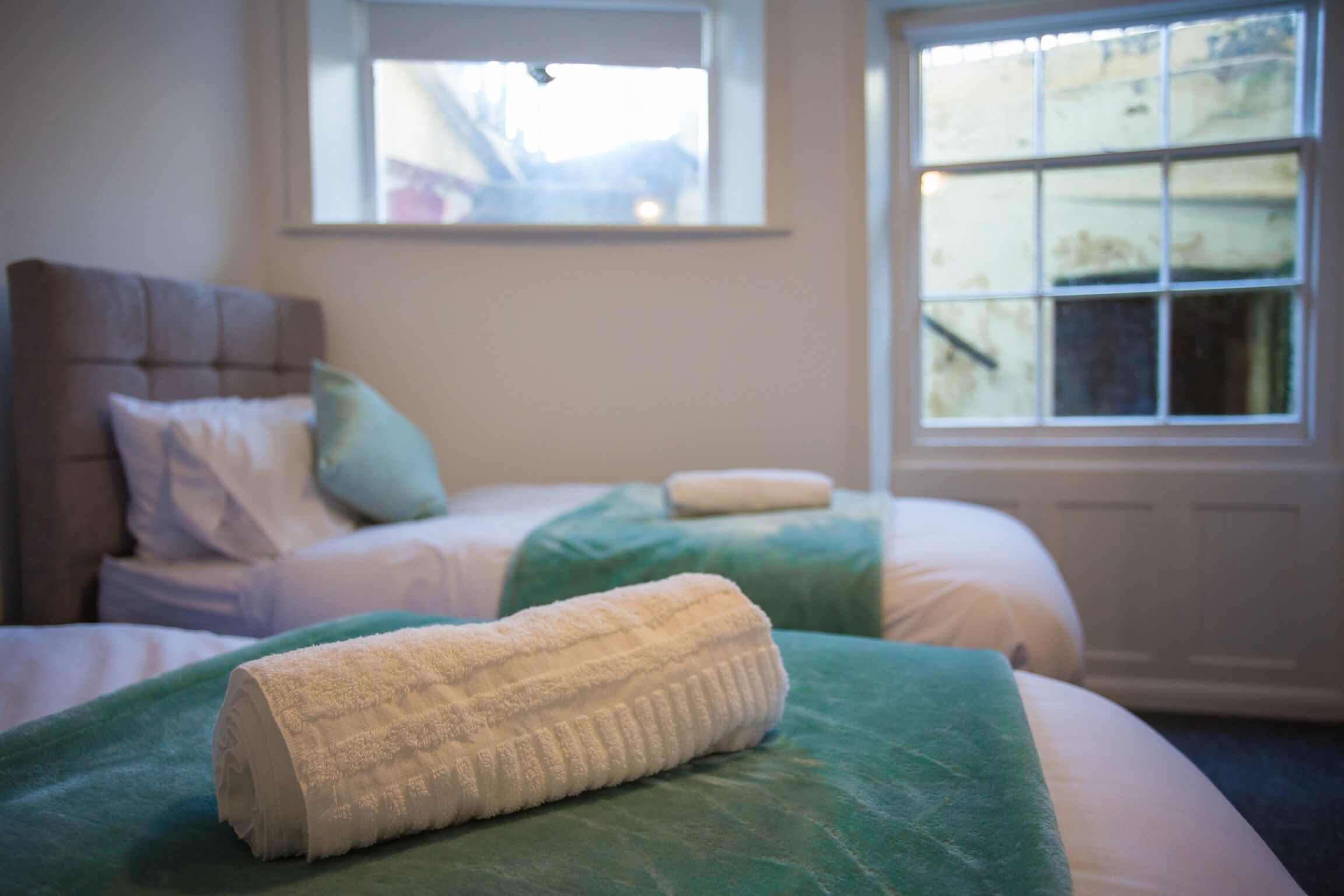 Un dormitorio con dos camas, cada una con cubrecama verde y almohadas blancas. Hay una ventana con vista a una montaña.