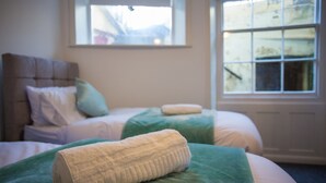Un dormitorio con dos camas, cada una con cubrecama verde y almohadas blancas. Hay una ventana con vista a una montaña.