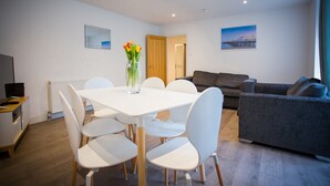 Una sala de estar moderna con una mesa de comedor blanca, sillas blancas, un sofá gris y un cuadro de un paisaje urbano en la pared.