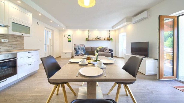 Une cuisine moderne avec des armoires blanches, un four encastré et un coin repas avec une table dressée pour quatre personnes.