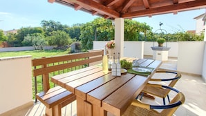 Une terrasse extérieure avec une table et des chaises en bois, un banc et un pot de fleurs suspendu.