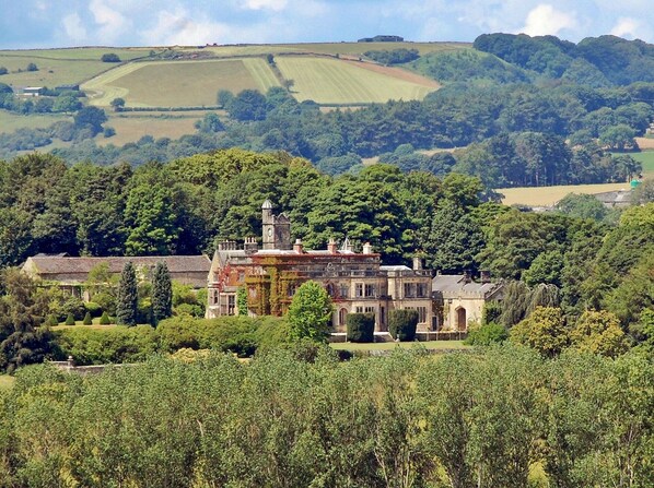 A historic building with a tower, surrounded by lush greenery and fields.