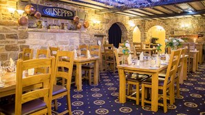 Een restaurantinterieur met stenen muren, houten tafels en stoelen, en een bord waarop 'Giuseppe's' staat.