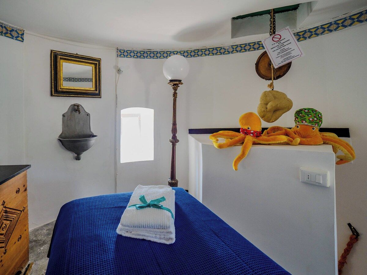 Una habitación con cama, una lámpara de pared, un espejo y una estantería con peluches.