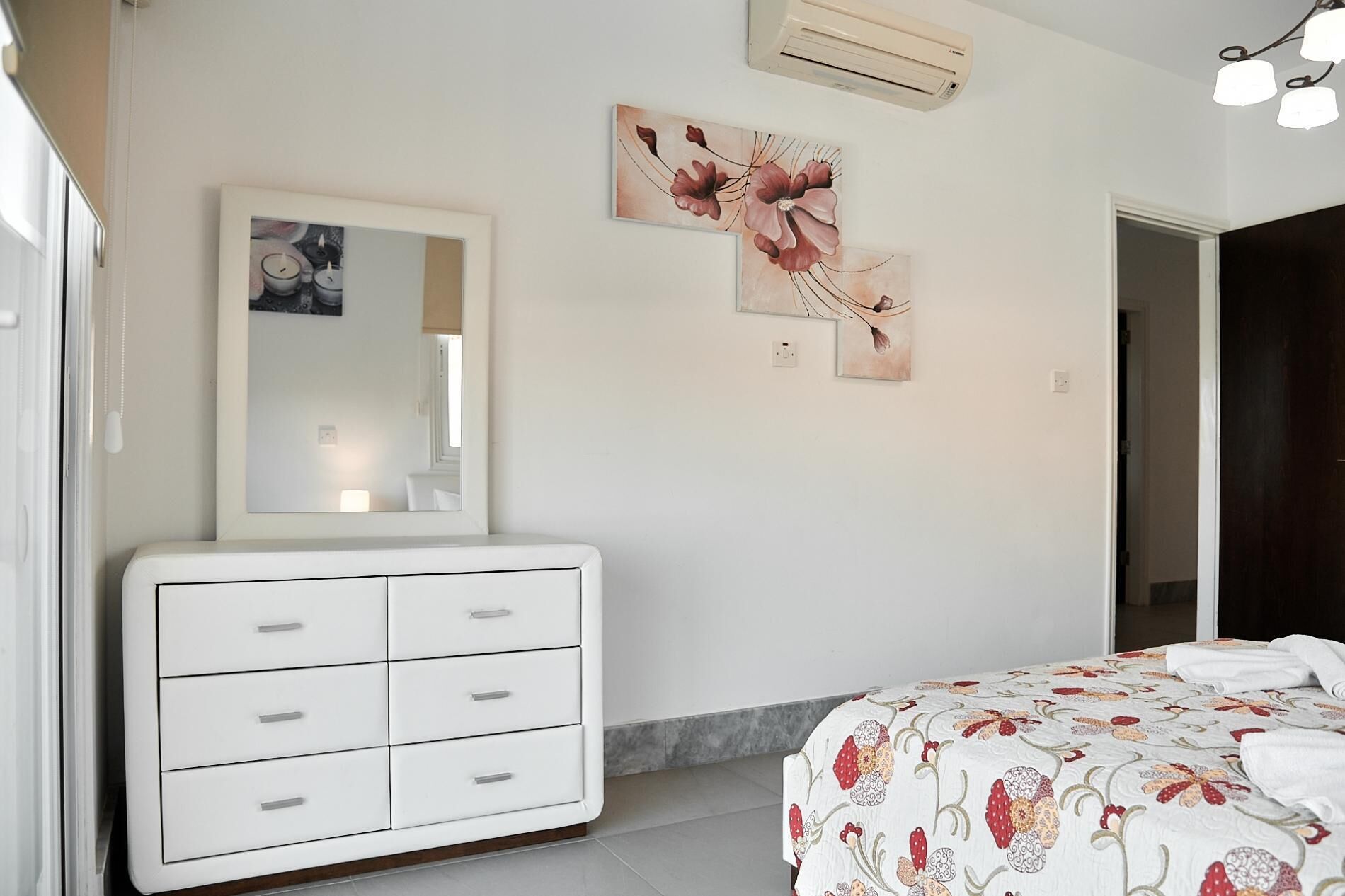 A bedroom with a white dresser, a bed with floral bedding, a mirror, and wall art.