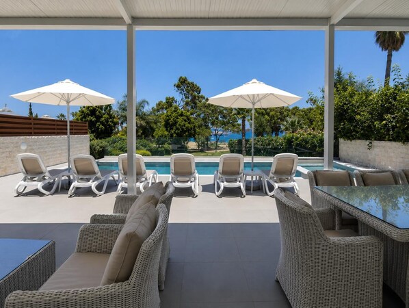 A poolside area with lounge chairs, umbrellas, and a glass table.