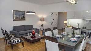 Una sala moderna con un sofá gris, una mesa de comedor lista para cuatro personas y una cocina al fondo.