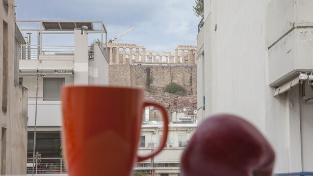 Una taza roja y un melocotón en un balcón con vistas a un paisaje urbano de arquitectura histórica.