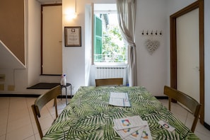Una habitación con cama, una mesa con papeles, una ventana con cortinas, una placa en la pared y un adorno con forma de corazón.