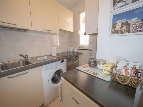 A compact kitchen with a washing machine, a sink, and a countertop with a basket of breakfast items.