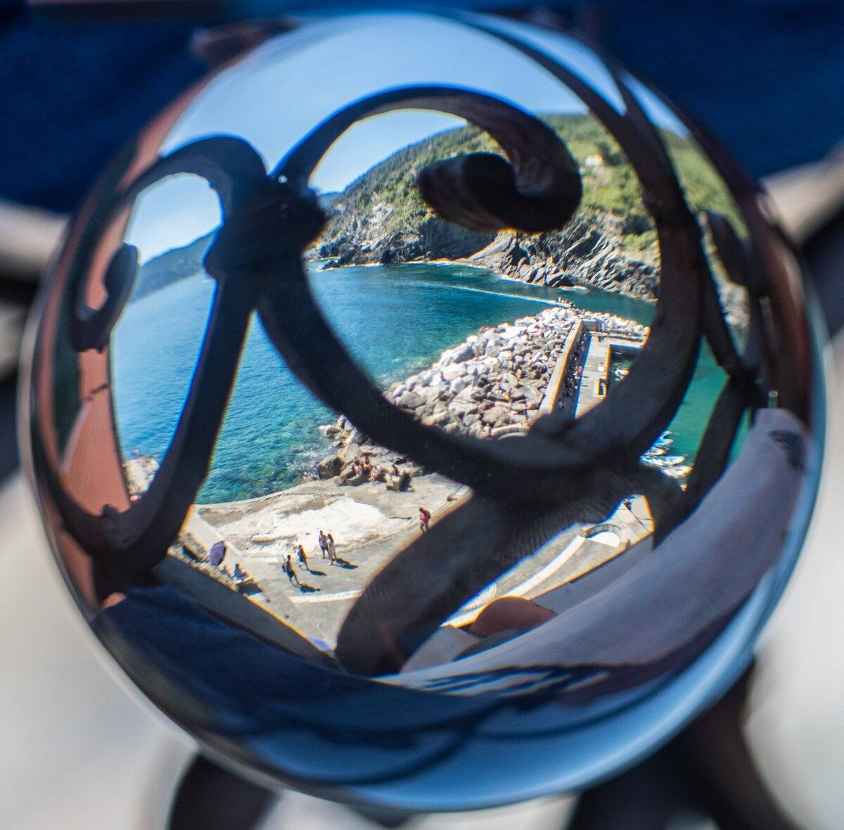A panoramic view through a circular object, capturing a coastal landscape with rocky terrain and a clear blue sea.