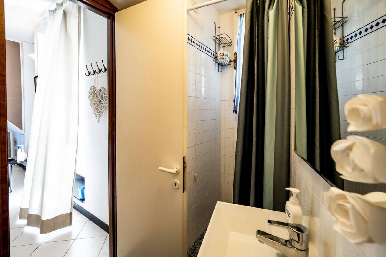 Un bagno con un lavandino bianco, zona doccia e specchio con porta asciugamani.