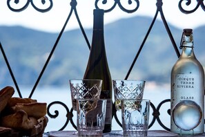 Una botella de Cinque Terre Riviera, dos vasos grabados y una botella de vino sobre una mesa con una barandilla metálica y un paisaje montañoso de fondo.