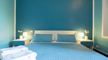 Une chambre d’hôtel avec un grand lit, deux tables de chevet avec des lampes et un mur bleu.