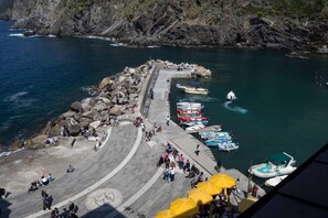 Zona costera con muelle de piedra, barcos y gente.