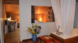 Una habitación con techo de madera, una ventana con vista a un dormitorio, un baño con cortina de ducha y una mesa con un jarrón de flores.