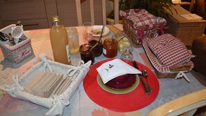 Una mesa de comedor dispuesta con platos, cubiertos y condimentos, rodeada de cestas de mimbre y una silla.