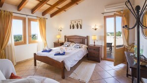 A bedroom with a wooden bed, two bedside tables with lamps, a view through the window, and a balcony door. - CAN MARINES - Villa with private pool in Calonge - Santanyí. Free WiFi. (Calonge)