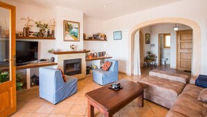 A living room with a TV, sofa, coffee table, and fireplace. There is a door leading to another room and a hallway with a door. - CAN MARINES - Villa with private pool in Calonge - Santanyí. Free WiFi. (Calonge)