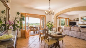 A spacious living area with a dining table, chairs, a sofa, and a TV. There is a balcony with a view of the greenery. - CAN MARINES - Villa with private pool in Calonge - Santanyí. Free WiFi. (Calonge)