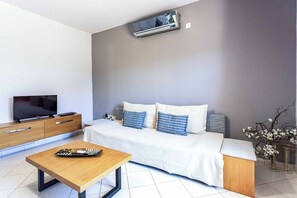 A modern hotel room with a flat-screen TV, a wooden bedside table, a sofa with blue and white pillows, and a vase with flowers.
