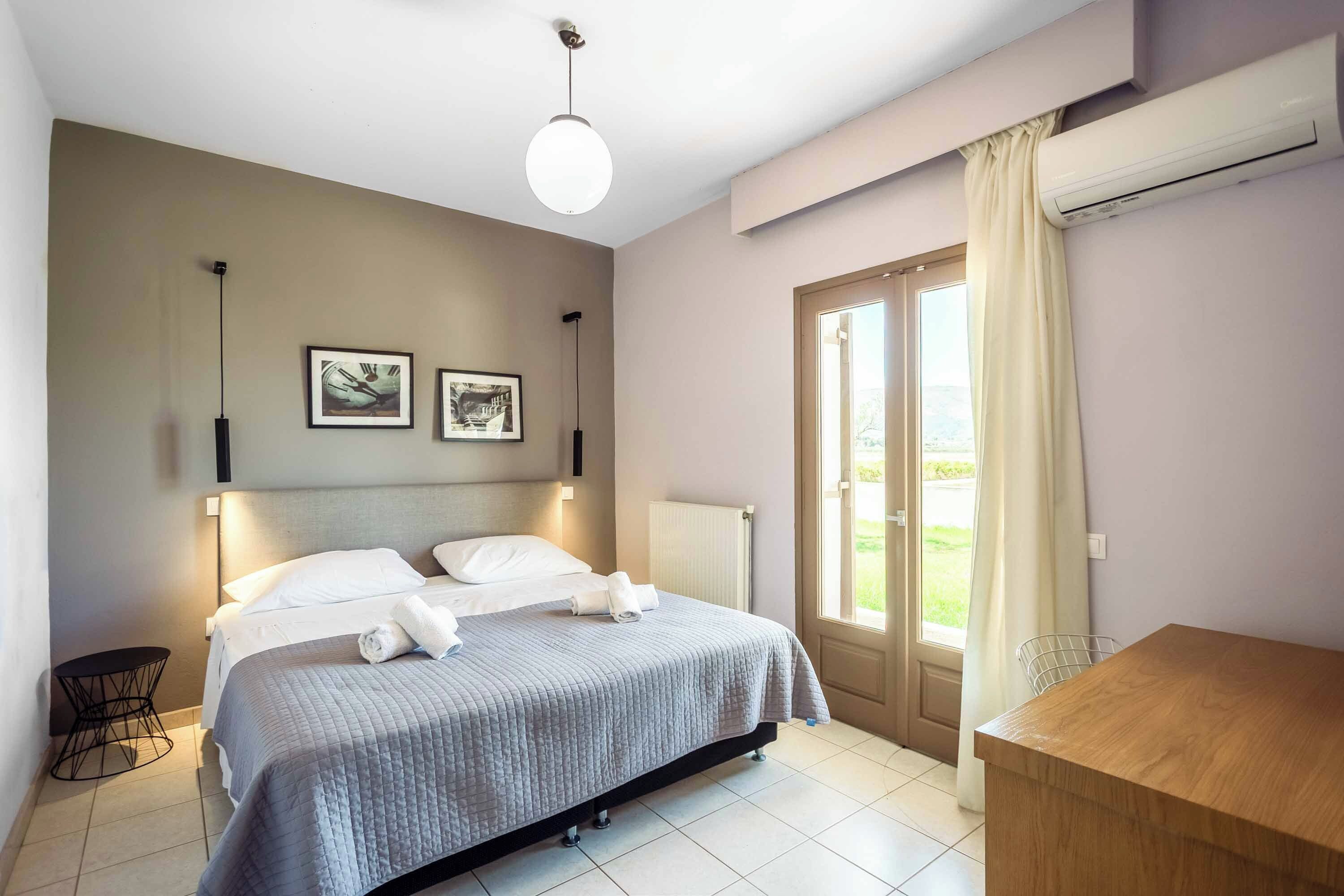 A hotel room with a bed, a desk, a radiator, and a window with curtains.