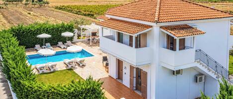A two-story house with a swimming pool, outdoor seating, and a view of the countryside.