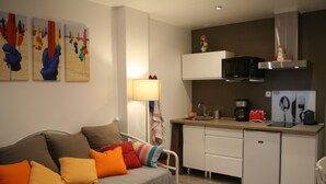 A compact living space with a kitchenette, a sofa with colorful cushions, a small dining table, and a microwave above the counter. - Gîte Côte Fleurie Lisieux center with parking (Lisieux)