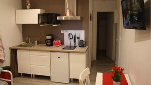 A compact kitchen with a microwave, toaster, and coffee maker. A small refrigerator is below the counter, and a TV is mounted on the wall. - Gîte Côte Fleurie Lisieux center with parking (Lisieux)
