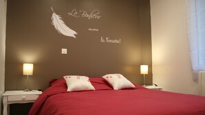A neatly made bed with red bedding and two pillows, a wall with a feather and text, and bedside lamps on nightstands. - Gîte Côte Fleurie Lisieux center with parking (Lisieux)