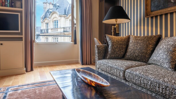 Un salón con sofá, una mesa de centro con un cuenco decorativo, una lámpara y vistas a un edificio a través de una ventana.