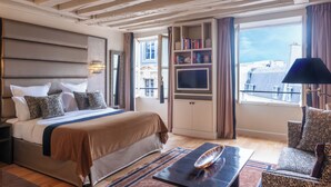 Una habitación de hotel con cama, televisión, estantería y vistas a edificios.