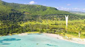 A coastal landscape with a beach, lush green hills, and a clear sky.