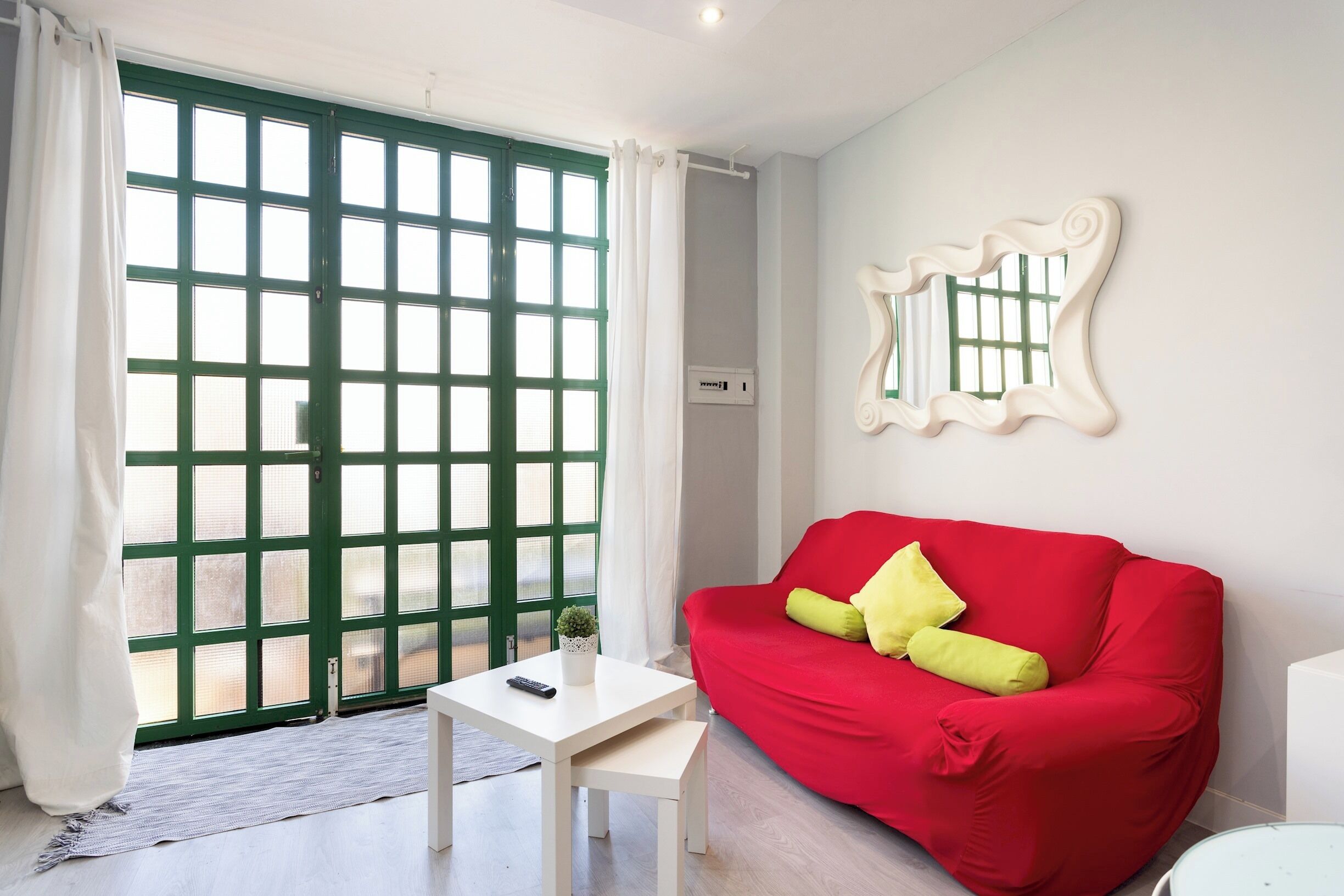 A room with a red sofa, a small table, a potted plant, and a large window with a green door.