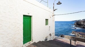 Ein weißes Gebäude mit grüner Tür und kleinem Fenster, das an eine felsige Küstenlinie und das Meer grenzt.