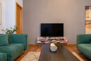 Ein Wohnzimmer mit Fernseher, Büchern und zwei grünen Sofas.