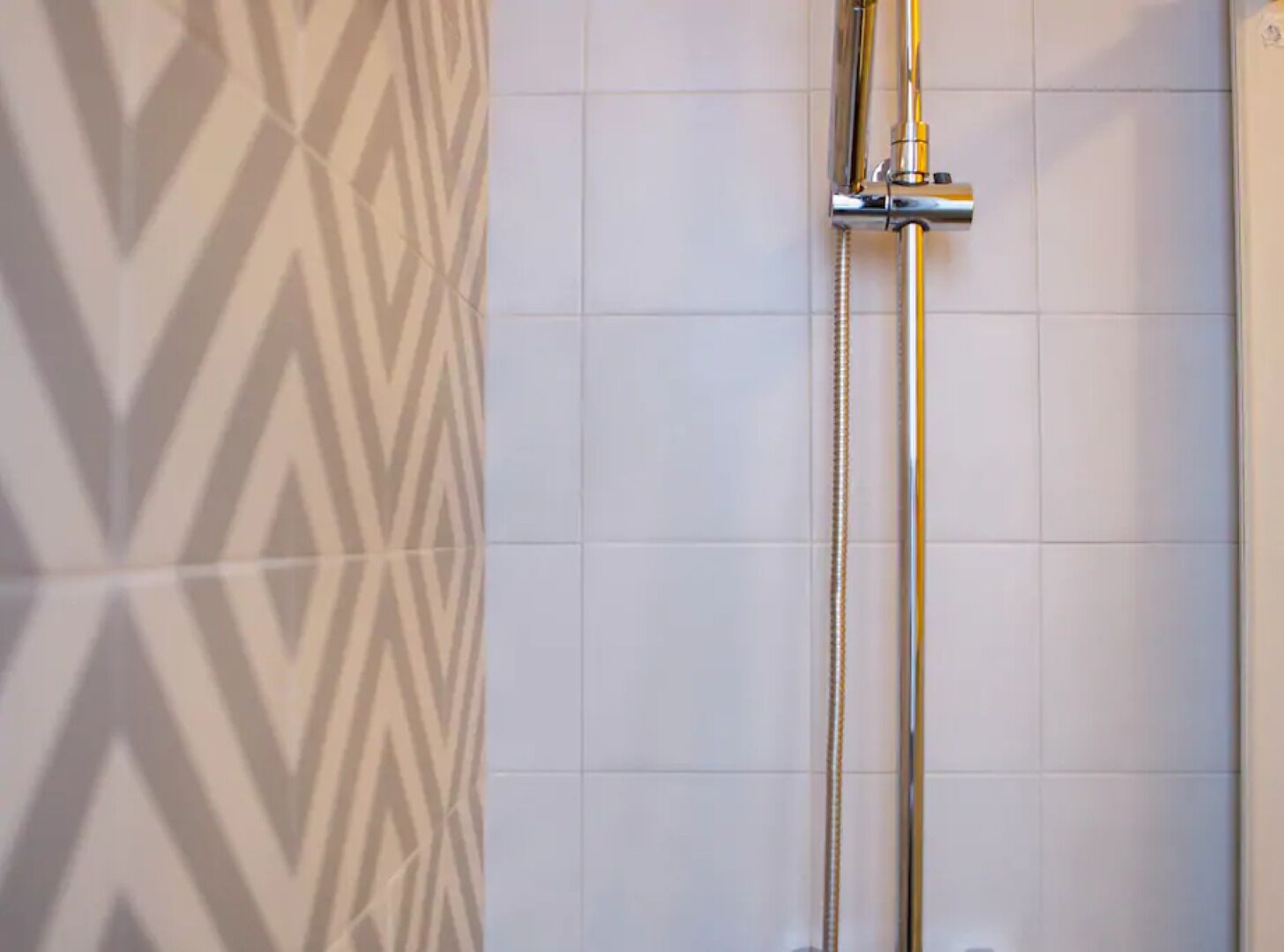 A shower with a chrome fixture and a patterned wall.
