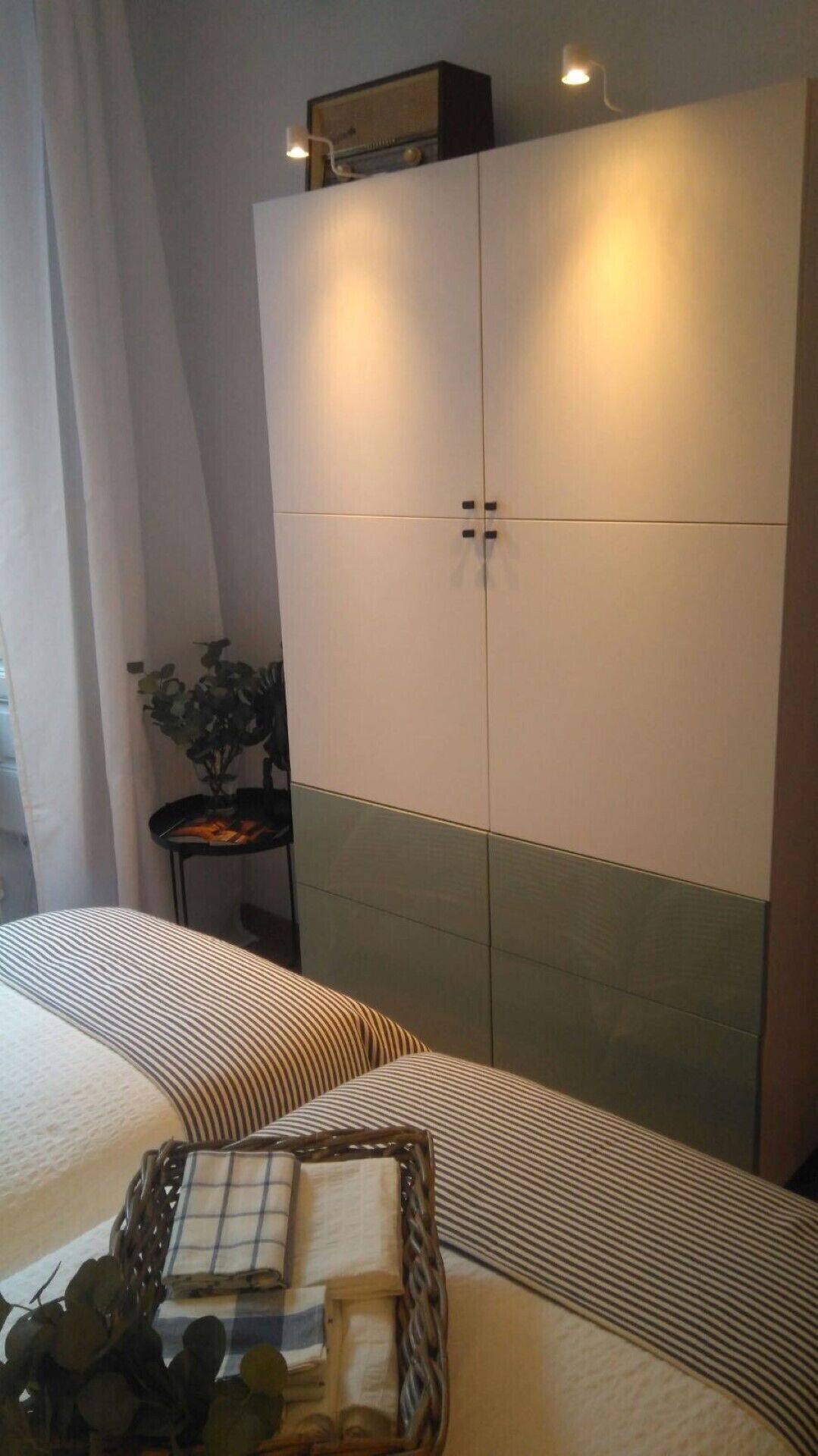 A bedroom with a bed, a bedside table with a lamp, a wardrobe, and a small potted plant.