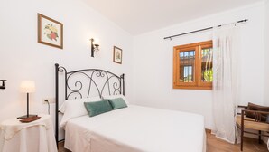 Un dormitorio ordenado con una cama individual, una mesita de noche con lámpara, una ventana con cortinas y una silla.