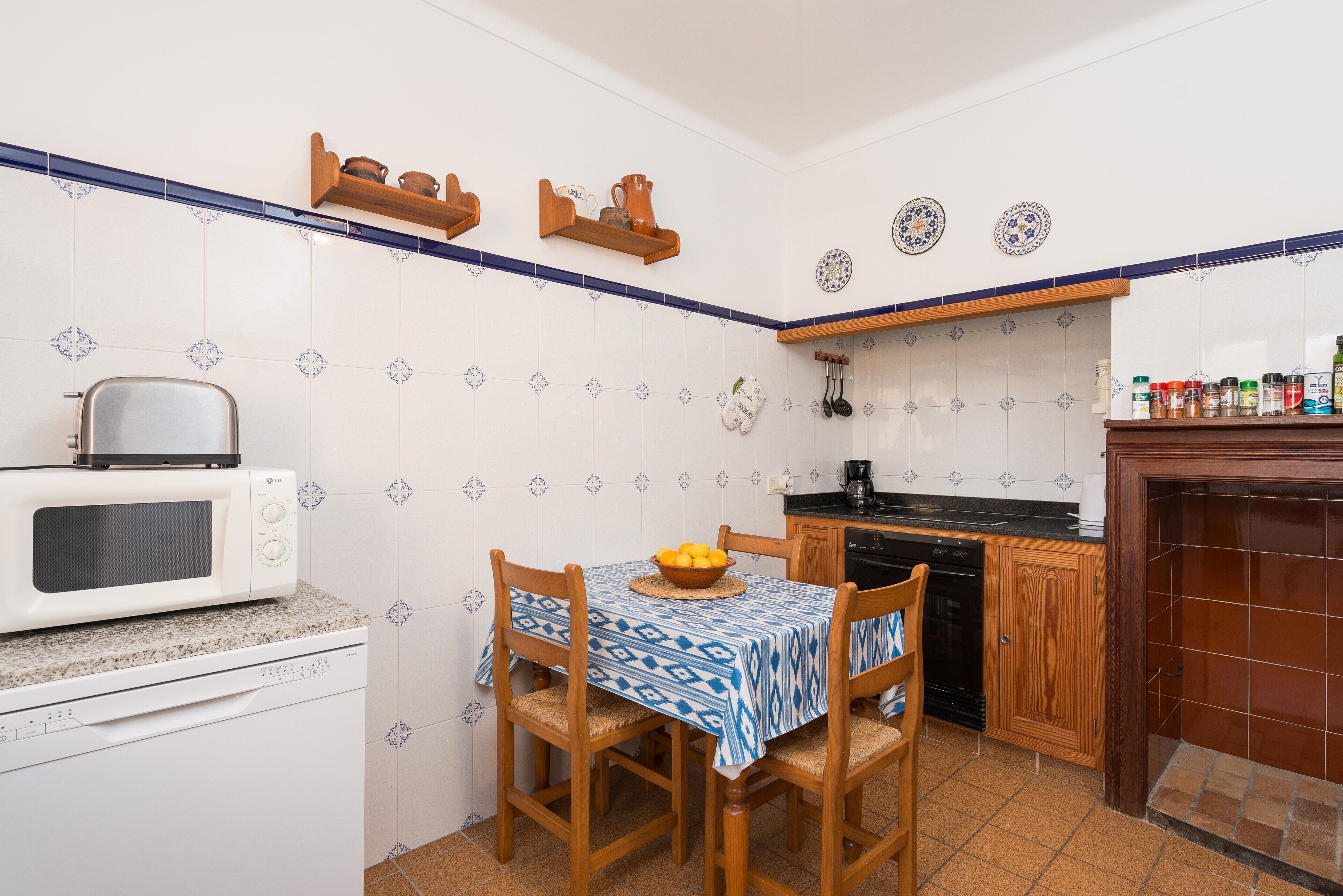 A compact kitchen with a microwave, wooden cabinets, and a dining table with a blue tablecloth.