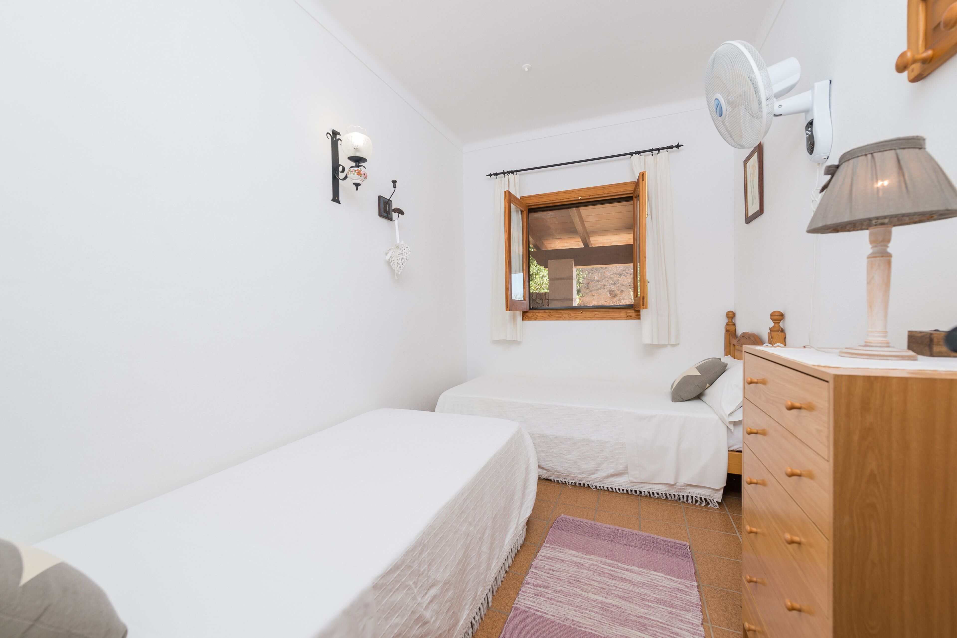 Een slaapkamer met twee eenpersoonsbedden, een houten dressoir, een plafondventilator en een raam met gordijnen.
