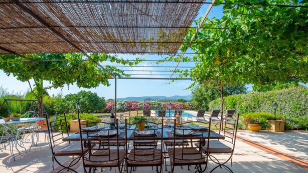 An outdoor dining area with tables and chairs, surrounded by greenery and a view of a pool and mountains. -  The Vignaux bastide (Grimaud)