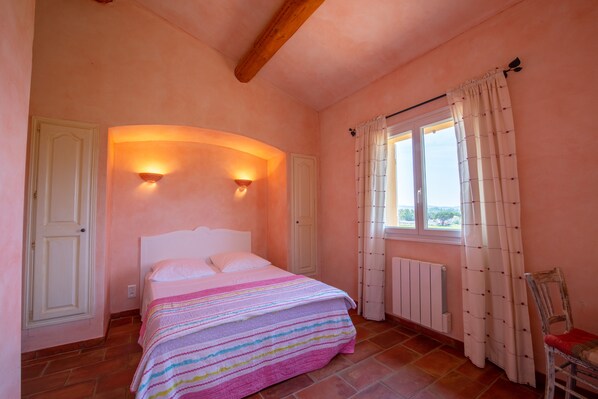 A bedroom with a bed, two wall-mounted lights, a window with curtains, a radiator, and a chair.