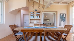 Un coin repas comprenant une table ronde en bois et six chaises, un buffet en bois avec des portes en verre, et un élément décoratif mural.