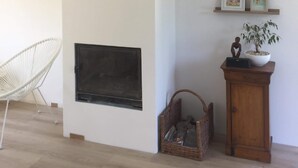 Een moderne woonkamer met een open haard, een witte stoel, een houten kast en wandplanken met ingekaderde foto's.