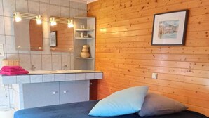 Een slaapkamer met een bed, een houten hoofdbord, een nachtkastje en een badkamer met een spiegel, wastafel en planken.