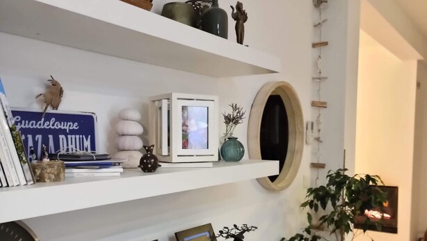 Een woonkamer met witte planken vol decoratieve objecten, een klok en ingelijste foto's.