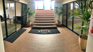 A hotel entrance with a wooden staircase, black mats, and potted plants.