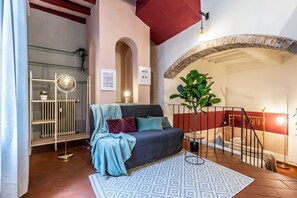 A cozy living room with a sofa, a patterned rug, a plant, and a staircase.