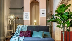 A cozy room with a sofa, a small round table, a radiator, and a large plant. - Wine Apartments Florence Vernaccia (Firenze)